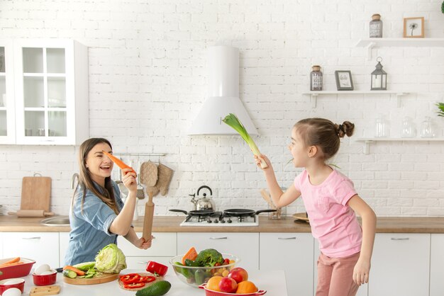 Mamá e hija preparan una ensalada en la cocina. Diviértete y juega con verduras.