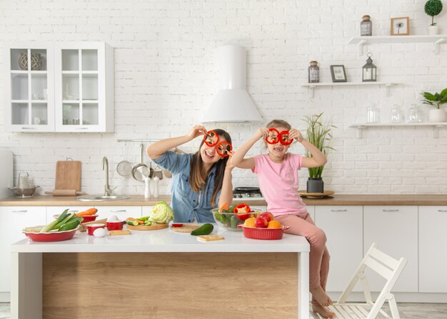 Mamá e hija preparan una ensalada en la cocina. Diviértete y juega con verduras