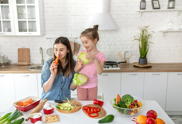 Mamá e hija preparan una ensalada en la cocina. Diviértete y juega con verduras