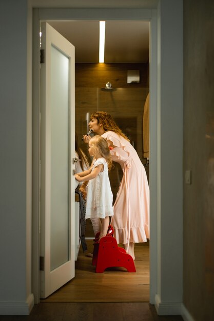 Mamá e hijas hacen maquillaje en el baño, aplican lápiz labial frente al espejo.