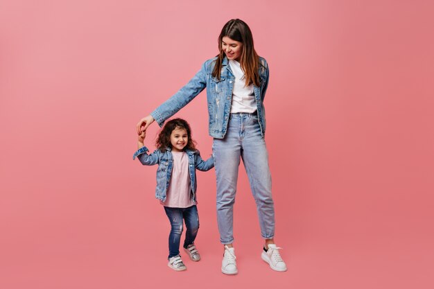 Mamá elegante bailando con hija preadolescente. Disparo de estudio de madre feliz y niño cogidos de la mano.