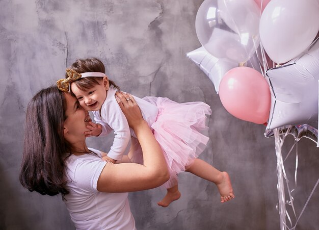 Mamá encantadora sostiene a su hijita tierna de pie en la habitación.