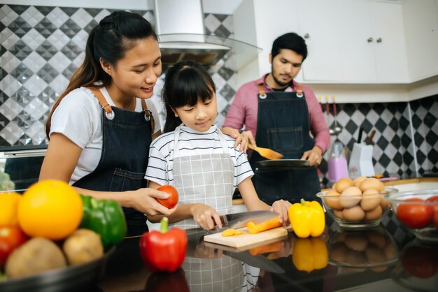 Mamá feliz le enseña a su hija a picar vegetales preparando ingredientes