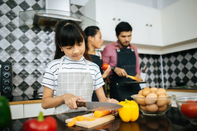 Mamá feliz le enseña a su hija a picar vegetales preparando ingredientes