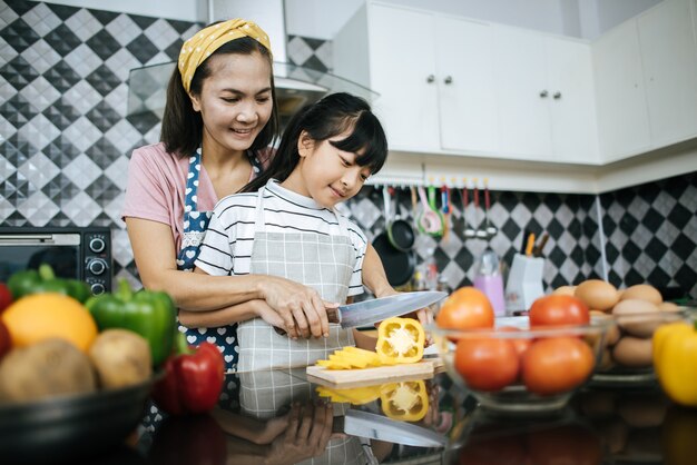 Mamá feliz que enseña a su hija que prepara y que taja la verdura para cocinar.