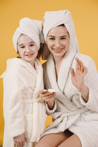 Mamá con hija. Chicas con albornoces blancos. Mamá enseña a su hija a maquillarse.