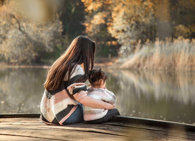 Mamá con hija pequeña en bosque otoñal.