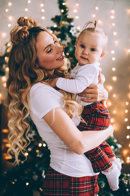 Mamá joven atractiva sostiene a un bebé de rodillas en un ambiente navideño