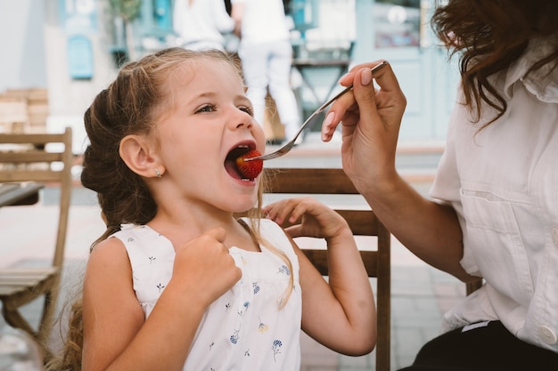 Mamá joven comiendo pastel con niño sonriente en la calle