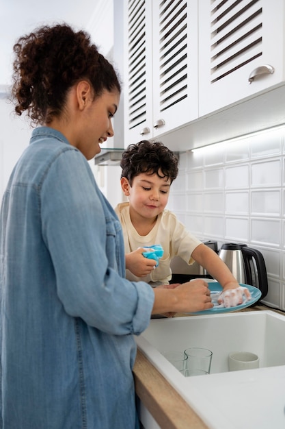 Mamá joven lavando platos con su hijo