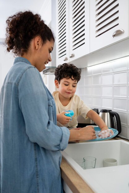 Mamá joven lavando platos con su hijo