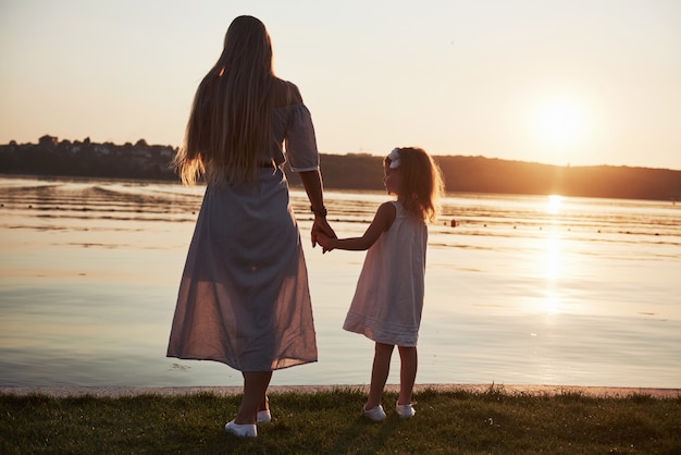 Mamá juega con su bebé de vacaciones cerca del océano, siluetas al atardecer