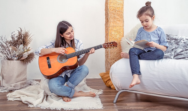 Mamá juega con sus hijas en casa. Lecciones de instrumento musical, guitarra. El concepto de amistad y familia de los niños.