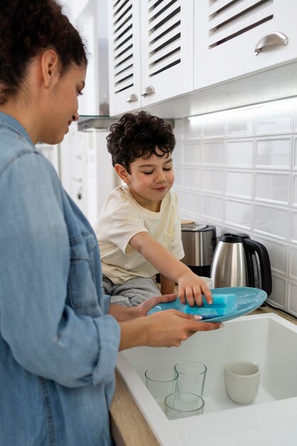 Mamá lavando platos con su hijo en la cocina