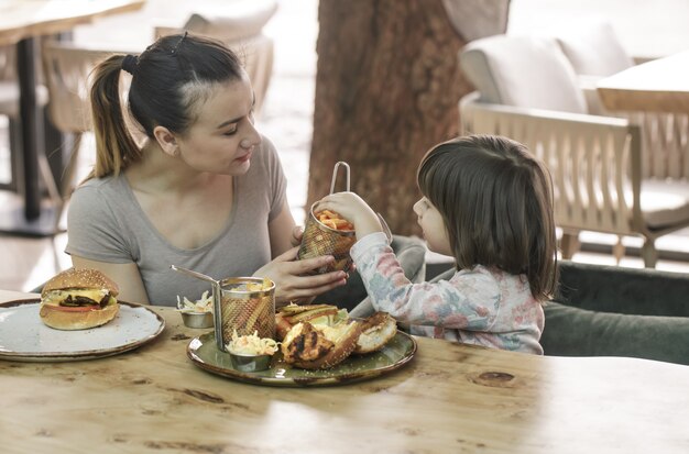 Mamá con una linda hija comiendo comida rápida en un café