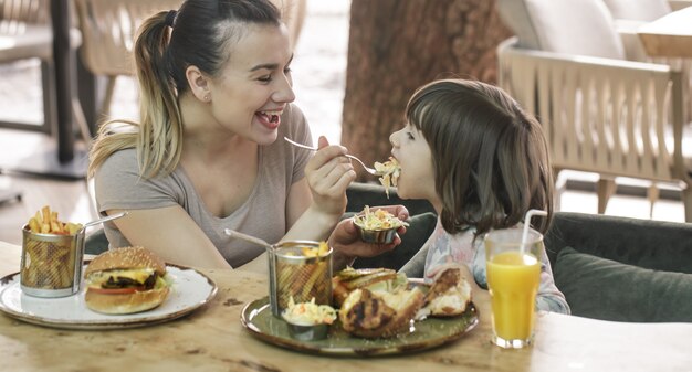 Mamá con una linda hija comiendo comida rápida en un café