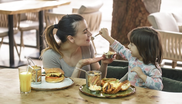 Mamá con una linda hija comiendo comida rápida en un café