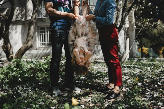 Mamá y papá juegan con la pequeña hija debajo de un árbol floreciente