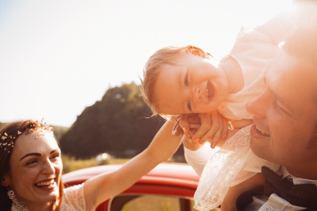 Mamá y papá juegan con su pequeña hija ante un auto rojo