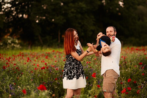 Mamá y papá sostienen a su pequeño hijo en los brazos que se colocan en el campo verde con amapolas