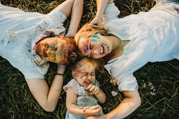 Mamá, papá y su hija cubiertos con pinturas de colores se encuentran en el césped verde