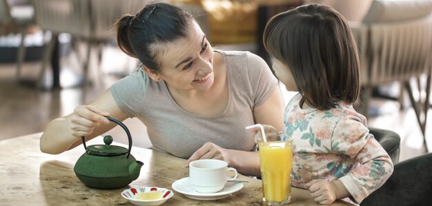 Mamá con una pequeña hija linda bebe té y jugo de naranja en un café, el concepto de valores familiares y familia