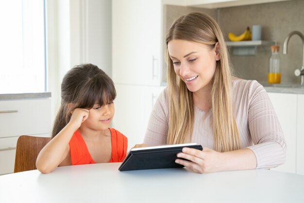 Mamá rubia sosteniendo la tableta y mostrándola a la hija.