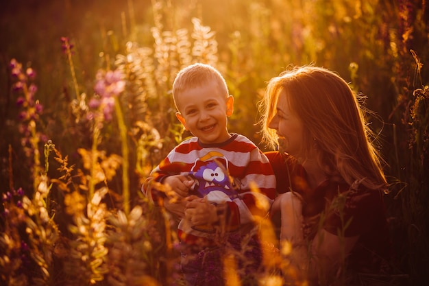 Mamá se sienta con su hijo en el campo a la luz del sol de la tarde