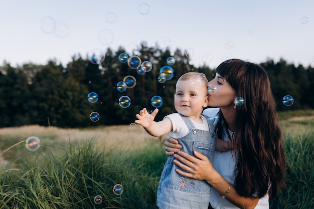 Mamá sostiene a la pequeña hija en sus brazos mientras los globos de jabón vuelan alrededor de ellos.