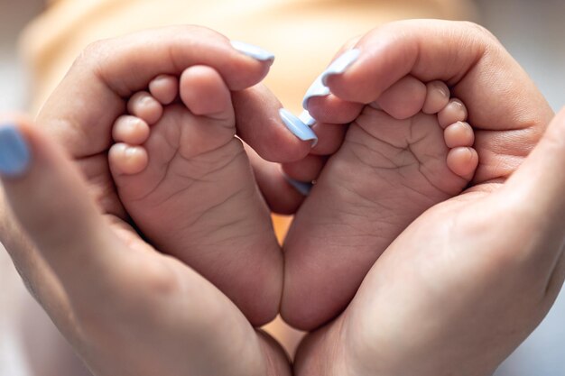 Mamá sostiene las piernas de un bebé recién nacido en sus manos