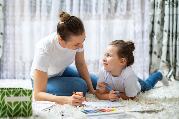 Mamá y su hija juegan juntas en casa en el piso. Feliz y sonriente