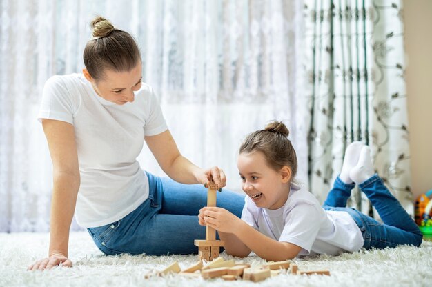 Mamá y su hija juegan juntas en casa en el piso. Feliz y sonriente