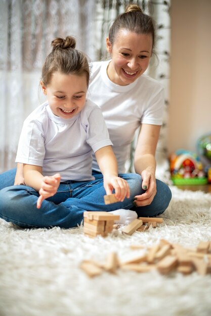 Mamá y su hija juegan juntas en casa en el piso. Feliz y sonriente