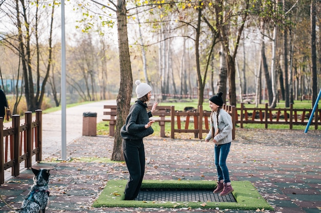 Mamá y su hija saltando juntas en el trampolín en el parque otoño