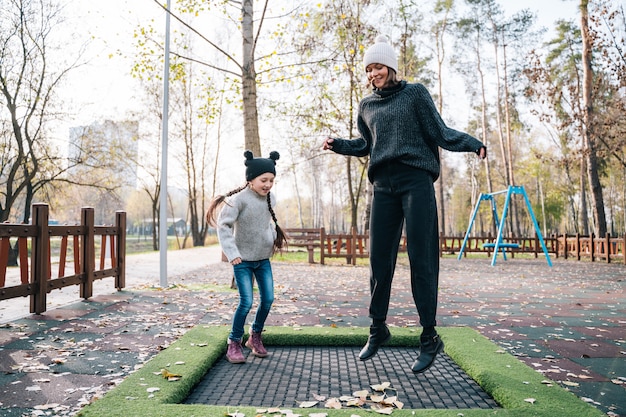 Mamá y su hija saltando juntas en el trampolín en el parque otoño