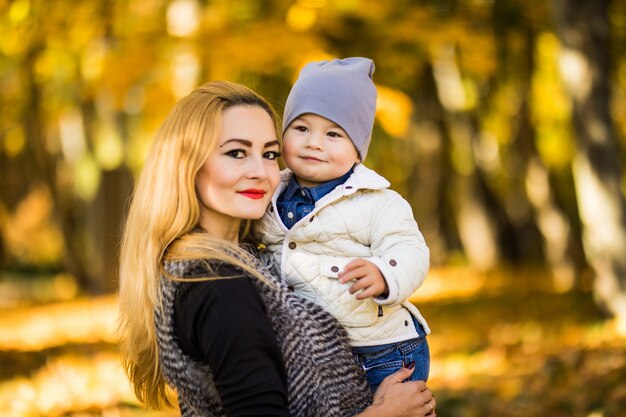 Mamá y su hijo están en el parque de otoño, al hijo le encanta mirar a su madre, la mujer tiene sus manos