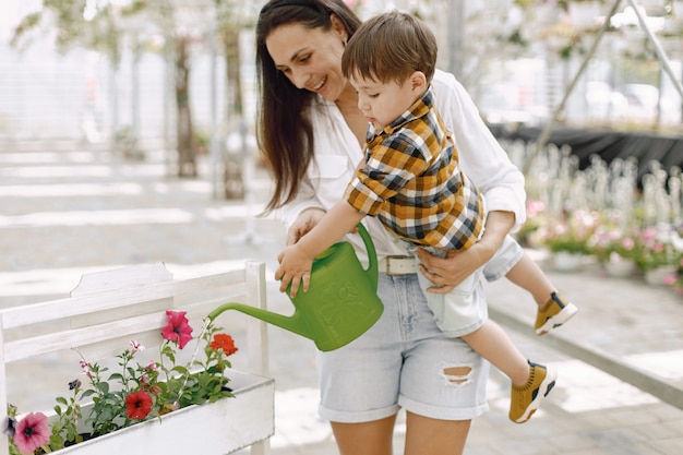 Foto gratuita mamá y su hijo con una lata de agua verde en el invernadero. niño niño regando flores en un invernadero