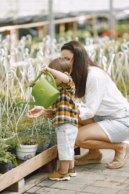 Mamá y su hijo con una regadera verde en el invernadero. Niño niño regando flores en un invernadero