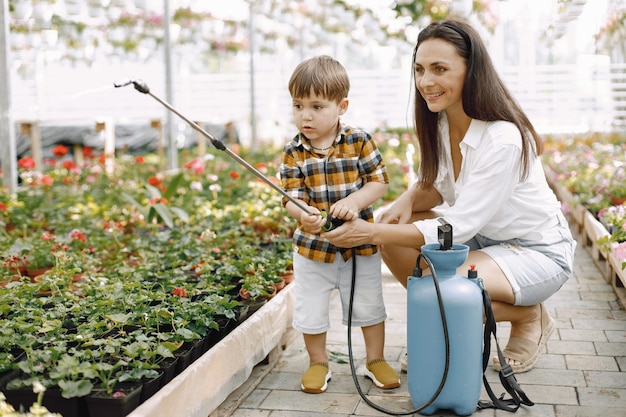 Mamá y su hijo con un rociador de agua azul en el invernadero. Niño niño regando flores en un invernadero