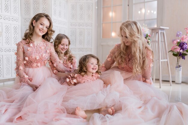 Mamá y tres hijas vestidas con galas rosas posan en una habitación blanca de lujo