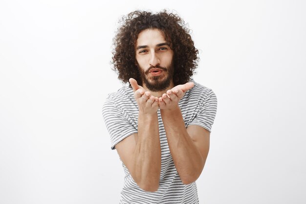 Mandando besos a mi amor. Retrato de encantador modelo masculino guapo con pelo rizado y barba