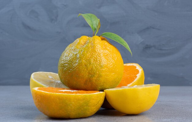 Mandarina entera sobre rodajas de limón y mandarina sobre fondo de mármol.