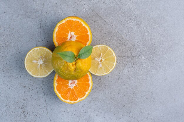 Mandarina entera sobre rodajas de limón y mandarina sobre fondo de mármol.