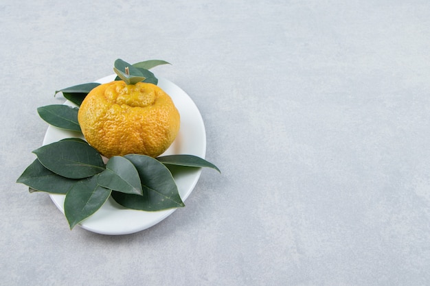 Mandarina madura sola con hojas en un plato blanco.