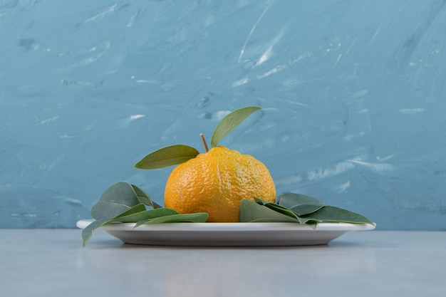 Mandarina madura solo con hojas en la placa blanca.