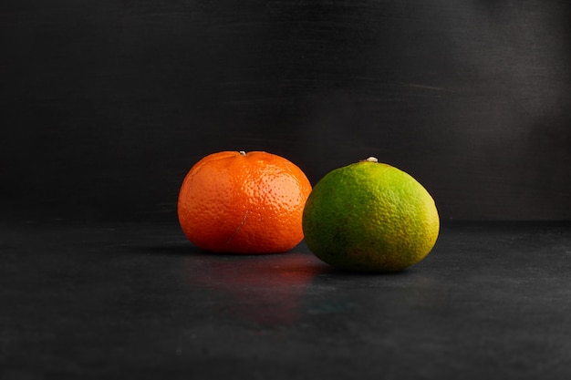 Mandarina y naranjas aisladas sobre fondo negro.