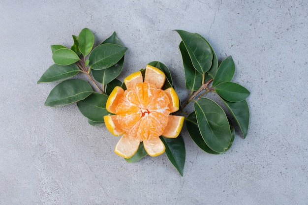 Mandarina pelada y hojas decorativas sobre fondo de mármol.