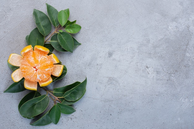 Foto gratuita mandarina pelada y hojas decorativas sobre fondo de mármol.