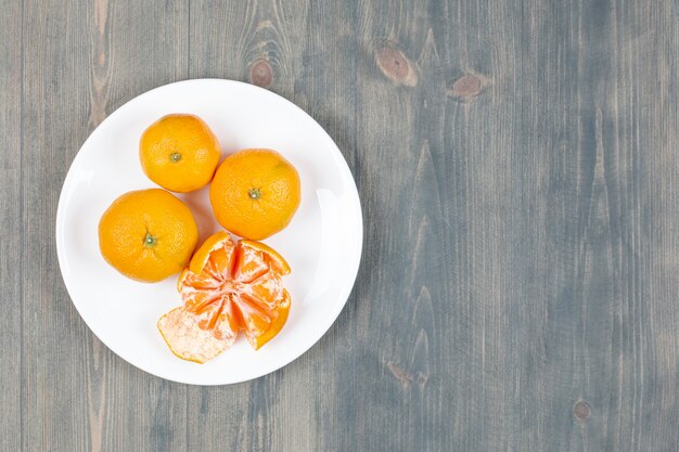 Mandarina pelada con mandarinas enteras en la placa blanca.