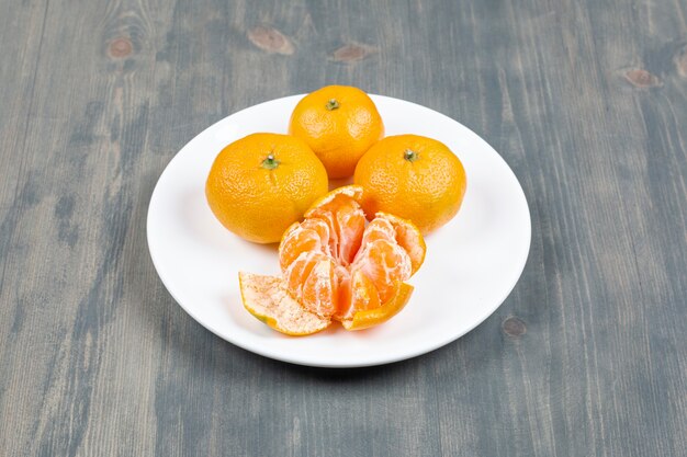 Mandarina pelada con mandarinas enteras en la placa blanca.